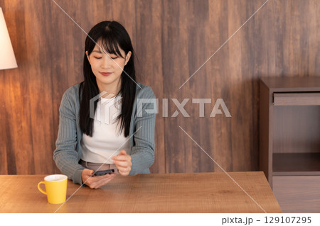 部屋でスマホを見る若い女性 129107295