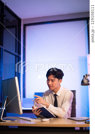 Businessman drinking coffee to get some energy for working overtime sitting at desk using computer and doing overtime 129108111