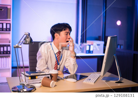 Businessman drinking coffee to get some energy for working overtime sitting at desk using computer and doing overtime Businessman drinking coffee to get some energy for working overtime sitting at desk using computer and doing overtime 129108131