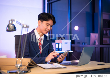 Businessman drinking coffee to get some energy for working overtime sitting at desk using computer and doing overtime 129108156