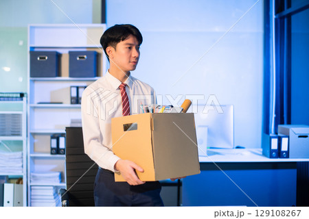 Asian male professional packing office belongings in a box, representing themes of resignation, new job, or relocation. Office, job, career change 129108267