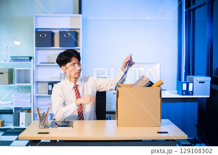 Asian male professional packing office belongings in a box, representing themes of resignation, new job, or relocation. Office, job, career change 129108302