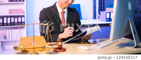 Young Asian lawyer at desk with legal scales and gavel, writing documents in office, offering legal services Young Asian lawyer at desk with legal scales and gavel, writing documents in office, offering legal services 129108317