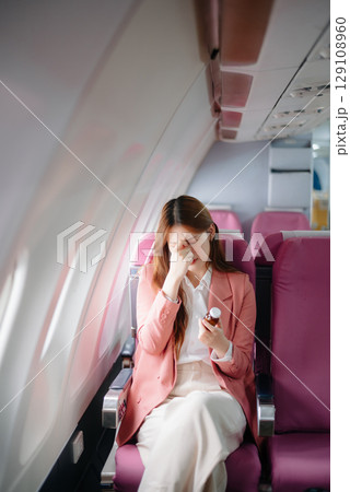Photo of a frustrated woman sitting on an airplane with her head in her hands. Asian woman sitting 129108960