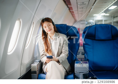 Portrait of a successful Asian businesswoman or entrepreneur in a formal suit on an airplane sitting in business class using a phone, computer laptop. Travel in style, work Portrait of a successful Asian businesswoman or entrepreneur in a formal suit on an airplane sitting in business class using a phone, computer laptop. Travel in style, work 129108986