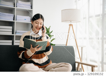 Young Asian woman listening music from headphones and writing note for her work idea in diary book.She in home office or cafe Young Asian woman listening music from headphones and writing note for her work idea in diary book.She in home office or cafe 129109132