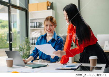 Two young Asian professionals engaged in teamwork and business discussions in modern office 129109334