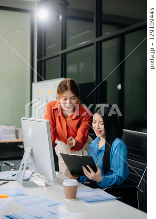 Two young Asian professionals engaged in teamwork and business discussions in modern office Two young Asian professionals engaged in teamwork and business discussions in modern office 129109445