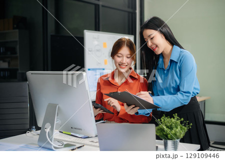 Two young Asian professionals engaged in teamwork and business discussions in modern office Two young Asian professionals engaged in teamwork and business discussions in modern office 129109446