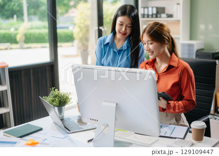 Two young Asian professionals engaged in teamwork and business discussions in modern office 129109447