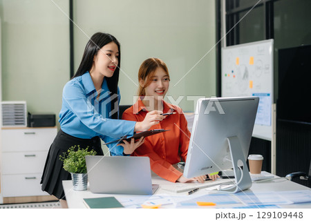 Two young Asian professionals engaged in teamwork and business discussions in modern office Two young Asian professionals engaged in teamwork and business discussions in modern office 129109448