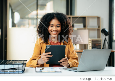 Young woman typing on tablet and laptop while sitting at the working in office 129109796