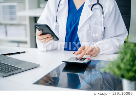 Healthcare costs and fees concept.Hand of smart doctor used a calculator and smartphone, tablet for medical costs at hospital Healthcare costs and fees concept.Hand of smart doctor used a calculator and smartphone, tablet for medical costs at hospital 129110099