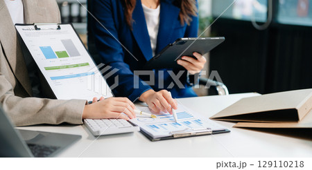 Business documents on office table with smart phone and calculator digital tablet and graph business with social network diagram and two colleagues discussing data working Business documents on office table with smart phone and calculator digital tablet and graph business with social network diagram and two colleagues discussing data working 129110218