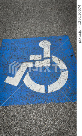 blue handicapped parking symbol painted on an asphalt surface, representing accessibility and inclusivity for people with disabilities. Rustic disabled parking sign 129110674