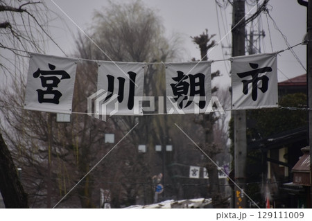 日本の岐阜県の高山市　春の高山祭期間中　宮川朝市の入口と案内幕　蕾状態の桜並木と曇空 129111009