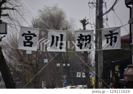 日本の岐阜県の高山市　春の高山祭期間中　宮川朝市の入口と案内幕　蕾状態の桜並木と曇空 129111029
