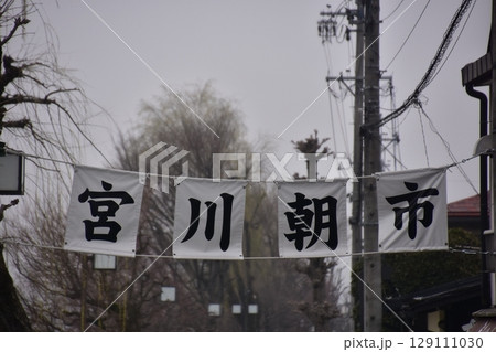 日本の岐阜県の高山市　春の高山祭期間中　宮川朝市の入口と案内幕　蕾状態の桜並木と曇空 129111030