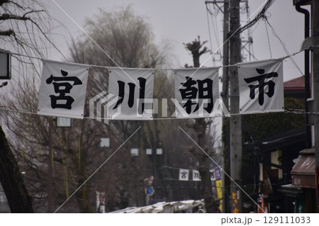 日本の岐阜県の高山市　春の高山祭期間中　宮川朝市の入口と案内幕　蕾状態の桜並木と曇空 129111033