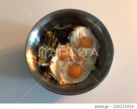 A colorful bowl of bibimbap with steamed rice, fresh vegetables, sliced meat, a fried egg, and a dollop of spicy gochujang. This iconic Korean dish offers a perfect mix of flavors and textures. 129111414