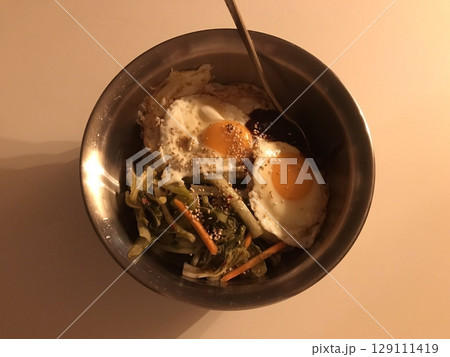 A colorful bowl of bibimbap with steamed rice, fresh vegetables, sliced meat, a fried egg, and a dollop of spicy gochujang. This iconic Korean dish offers a perfect mix of flavors and textures. 129111419