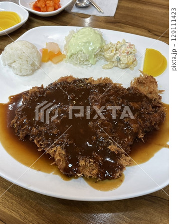 Crispy tonkatsu, a Japanese-style breaded and deep-fried pork cutlet, served with shredded cabbage and drizzled with savory sauce. A delightful balance of crunchy texture and juicy meat. 129111423