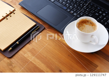 リング式のシステム手帳を広げ、コーヒー(カフェ・ラテ)を飲みながらパソコンでデスクワーク中のイメージ リング式のシステム手帳を広げ、コーヒー(カフェ・ラテ)を飲みながらパソコンでデスクワーク中のイメージ 129111747