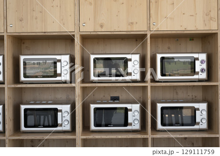 Modern kitchen display showcases various microwave models in a minimalistic wooden shelving unit 129111759
