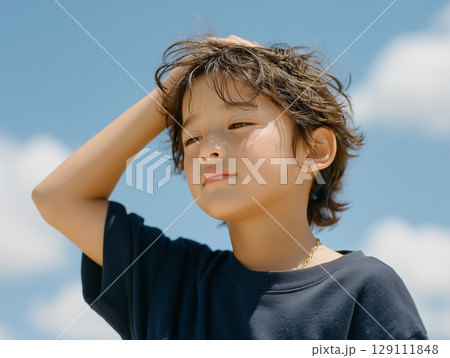 暑さで額に手を当てる男の子の夏の一場面 129111848