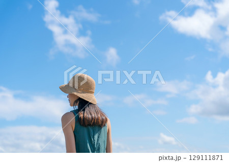 青空と麦わら帽子をかぶった女性 129111871