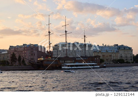 A Historic Ship is Gracefully Docked by Stunning City Buildings as the Sun Sets Beautifully 129112144