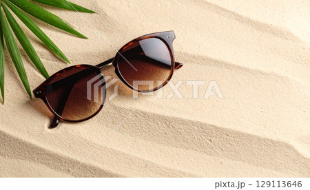 Fashionable black sunglasses with retro plastic frame and dark lenses, isolated on a white sand beach with the summer sun 129113646