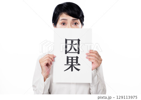 因果と書かれた紙を持つ中年女性 129113975