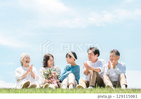 青空の見える公園・丘に座る家族・親子・三世代家族（父親・母親・娘・祖母・祖父） 129115061