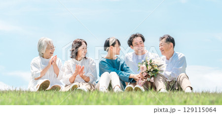 青空の見える公園・丘に座る家族・親子・三世代家族（父親・母親・娘・祖母・祖父） 129115064