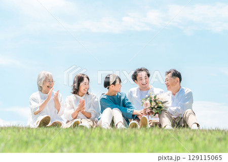 青空の見える公園・丘に座る家族・親子・三世代家族(父親・母親・娘・祖母・祖父) 青空の見える公園・丘に座る家族・親子・三世代家族(父親・母親・娘・祖母・祖父) 129115065