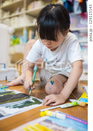 床に座って真剣に絵を描く子ども 129115143