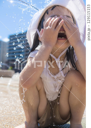 夏の日差しの中で噴水で水遊びを楽しむ子ども 129115153