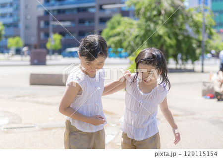 噴水の広場で水しぶきを浴びながら遊ぶ女の子 129115154