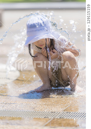 噴水の広場で水しぶきを浴びながら遊ぶ女の子 129115159