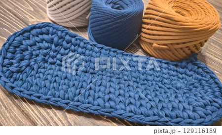 The bottom of the bag is crocheted from blue knitted yarn On a wooden background The bottom of the bag is crocheted from blue knitted yarn On a wooden background 129116189
