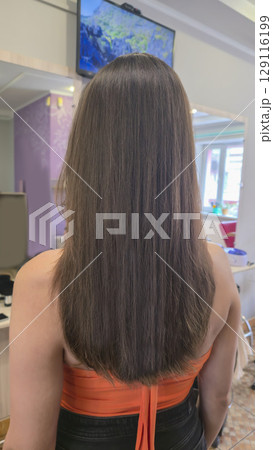 Woman with long brown dyed hair stands with her back in a beauty salon. Brunette Woman with long brown dyed hair stands with her back in a beauty salon. Brunette 129116199