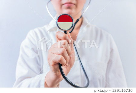 Female doctor holding stethoscope with Indonesia flag. National health system of Indonesia Female doctor holding stethoscope with Indonesia flag. National health system of Indonesia 129116730