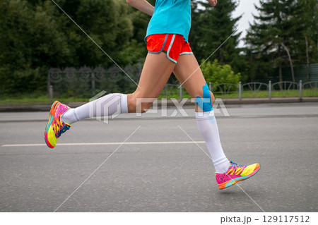 female athletes runnnig marathon, legs in white compression socks and kinesio tape on her knee female athletes runnnig marathon, legs in white compression socks and kinesio tape on her knee 129117512