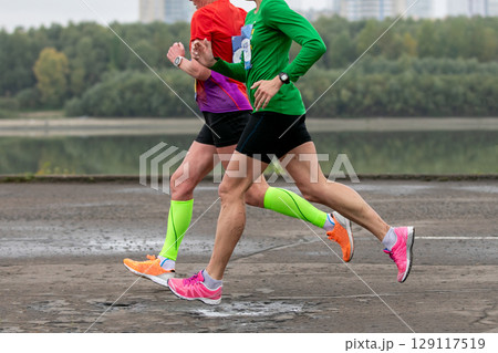 two female athletes running along river embankment marathon race 129117519