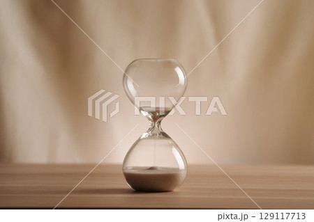 A simple hourglass on a wooden table with a beige backdrop, symbolizing time flow and minimalistic living. Running out of time, uncluttered presentation for stylish concepts. A simple hourglass on a wooden table with a beige backdrop, symbolizing time flow and minimalistic living. Running out of time, uncluttered presentation for stylish concepts. 129117713