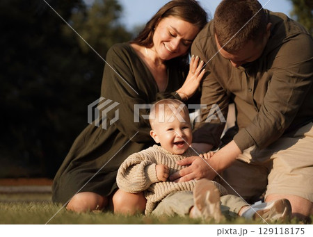 happy loving family with baby son sitting on grass in park happy loving family with baby son sitting on grass in park 129118175
