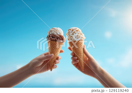 hands holding vanilla and chocolate icecream cones. blue sky on background 129119240