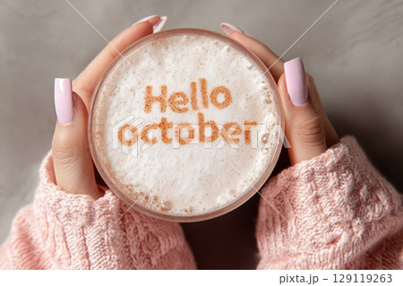 woman hands in pink knit sweater holding cup of coffee with crema. Text Hello october on it. 129119263