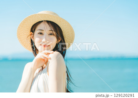 海と青空バックの麦わら帽子を被った女性 129120291